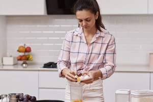 young woman preparing dough and cracking eggs