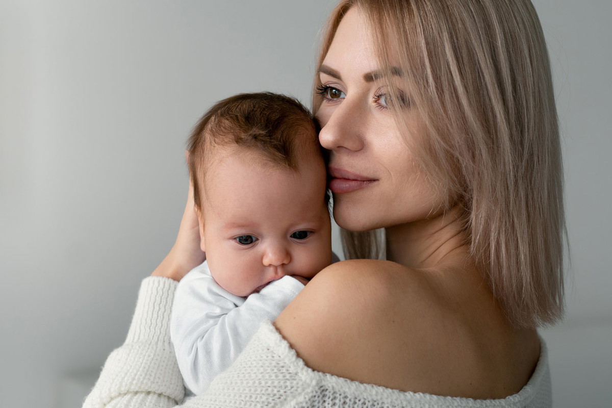 Mom is standing, holding and hugging her newborn baby. Her lips gently brush against his cheek.