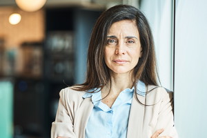 kobieta w wieku 45 plus z długimi ciemnymi włosami stoi zmartwiona i smutna na tle biura