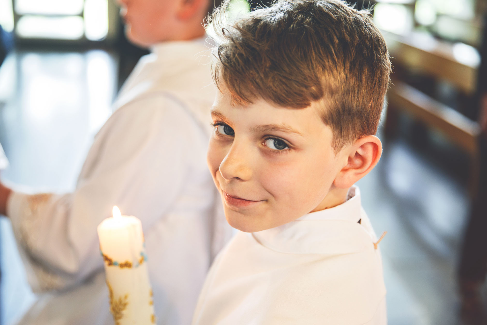 Little kid boy receiving his first holy communion. Happy child holding Christening candle. Tradition in catholic curch. Kid in a white traditional gown in a church near altar.