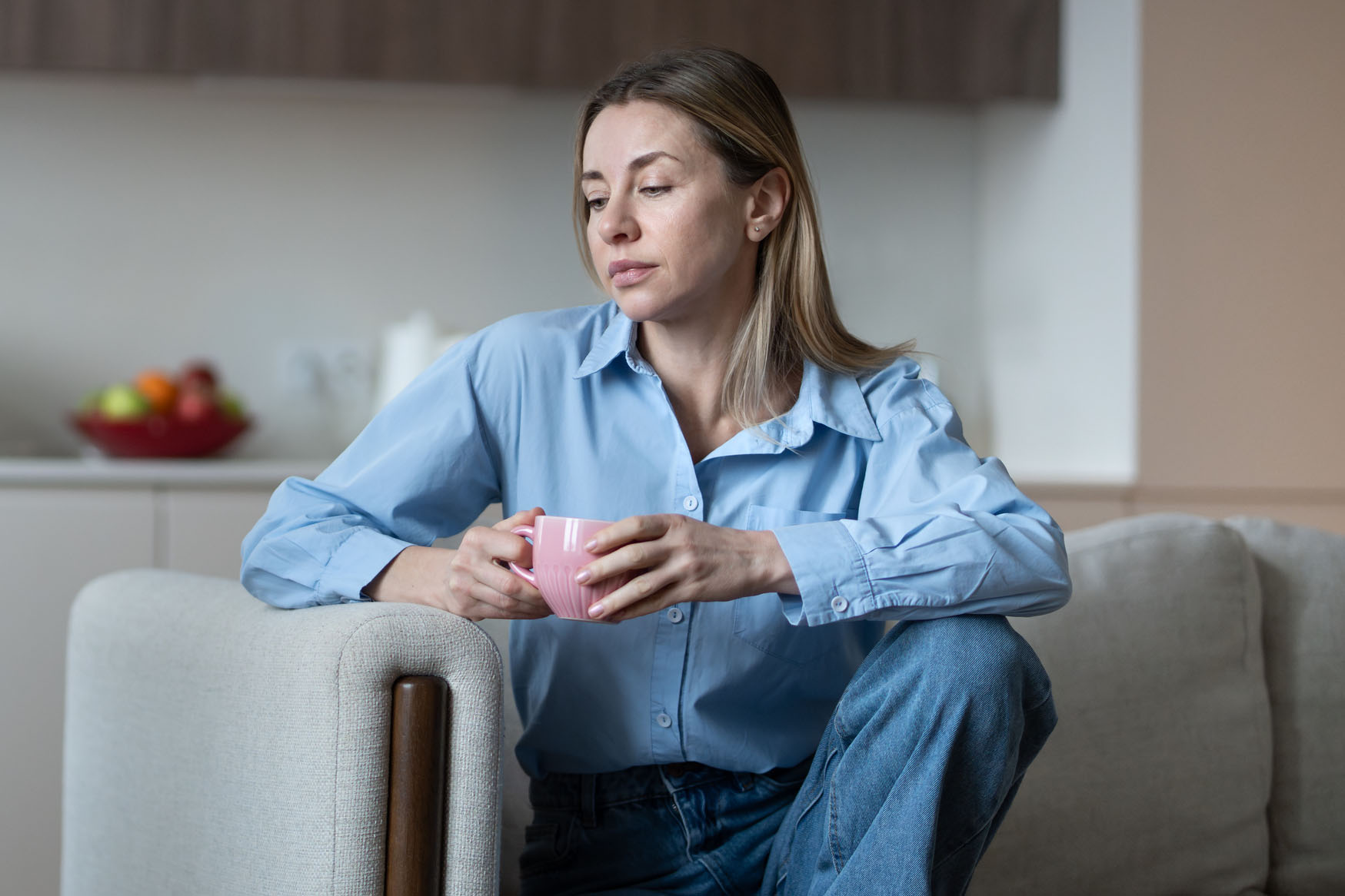 Melancholic lonely middle aged woman resting at home couch with coffee mug, deep in thought.