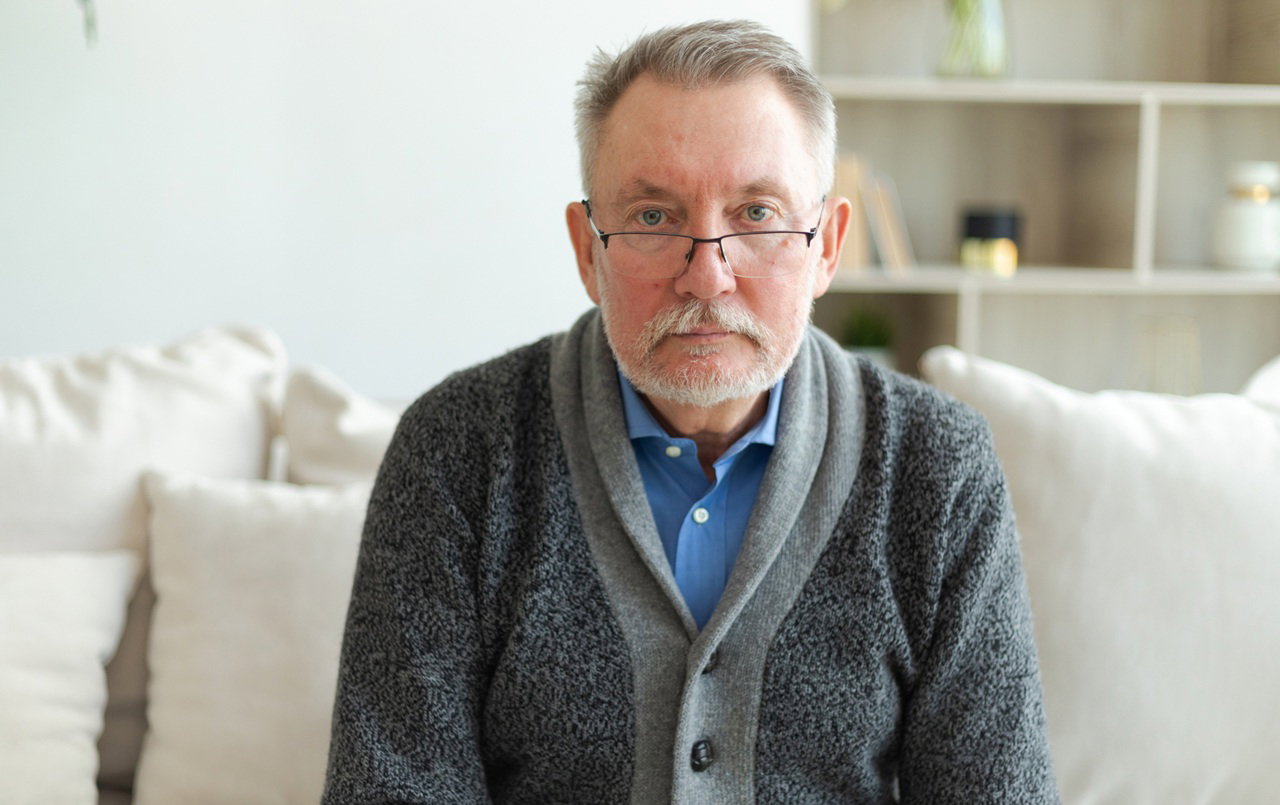 mężczyzna w wieku 65 plus w okularach siedzi na kanapie smutny i zamyślony