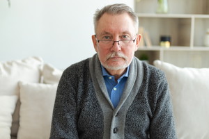 mężczyzna w wieku 65 plus w okularach siedzi na kanapie smutny i zamyślony
