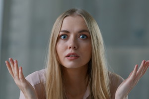 kobieta w wieku 30 plus blondynka z długimi włosami siedzi zdziwiona i podminowana podnosząc ręce w górę