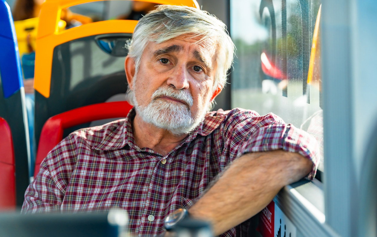 mężczyzna w wieku 60 plus siwy siedzi w autobusie miejskim ze smutną miną zmartwiony