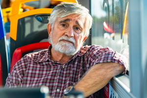 mężczyzna w wieku 60 plus siwy siedzi w autobusie miejskim ze smutną miną zmartwiony