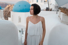 kobieta w wieku 30 plus w białej sukience stoi na tle pejzażu Santorini w Grecji smutna i zamyślona
