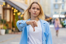 młoda kobieta w wieku 30 plus blondynka w niebieskiej marynarce stoi na ulicy niezadowlona i pokazuje kciuk w dół