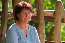kobieta w wieku 60 plus siedzi przy drewnianym płocie w niebieskiej bluzeczce zamyślona i smutna