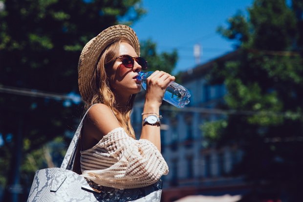 Stylish woman drinking a water from bottle, outdoors.