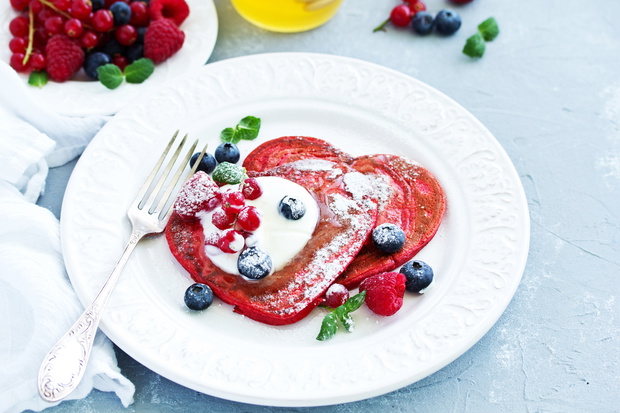 Pancakes red velvet in the form of a heart with berries and crea