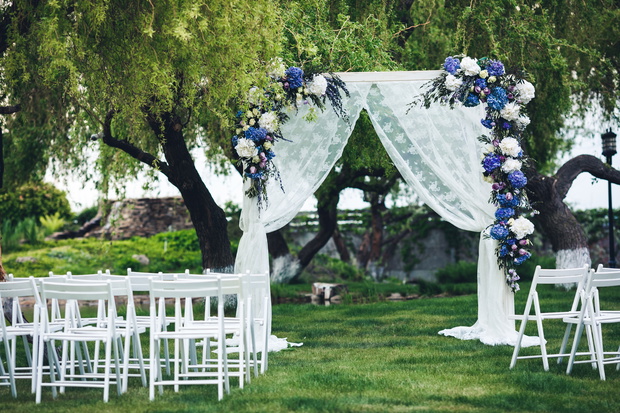 The wedding arch is decorated with fabric and flowers, chairs for guests. Wedding ceremony in nature.