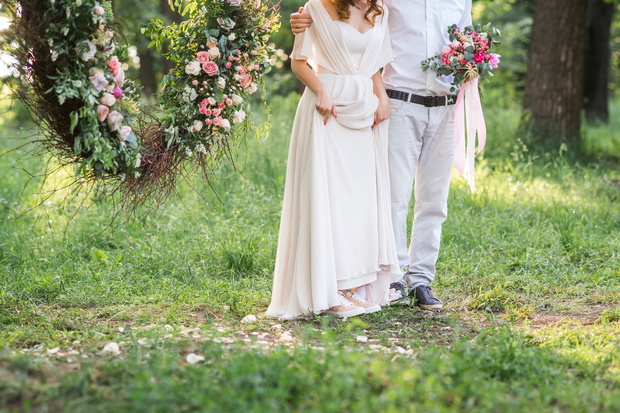 A beautiful bride to the background of a round arch. Fragment. Wedding bouquet and bride's hands