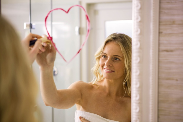 Beautiful blonde drawing big heart on mirror