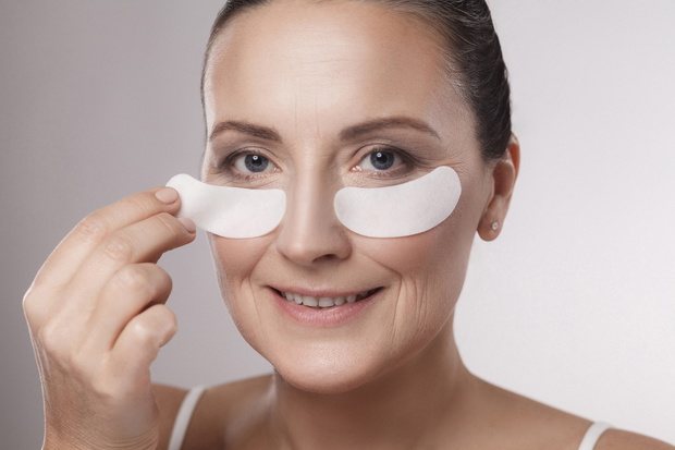Closeup portrait of beautiful middle aged woman with perfect skin using white hydrogel patches with lifting anti-wrinkle collagen effect, gray background, indoor, studio shot, copy space, isolated