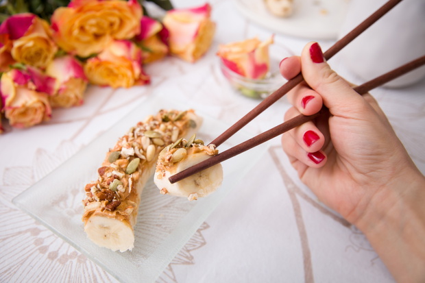 Banana sushi servered with nuts and granola on a glass plate. Ha