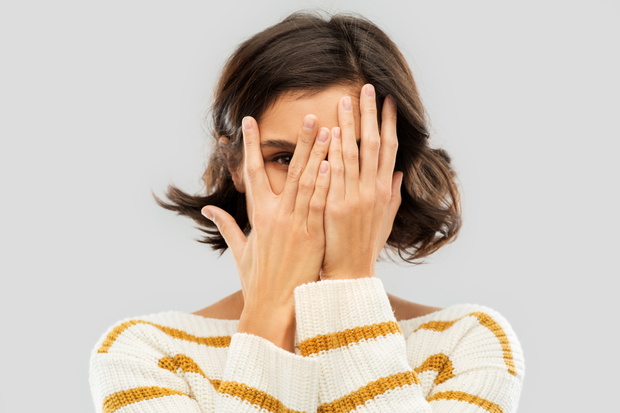 young woman looking by one eye through her fingers