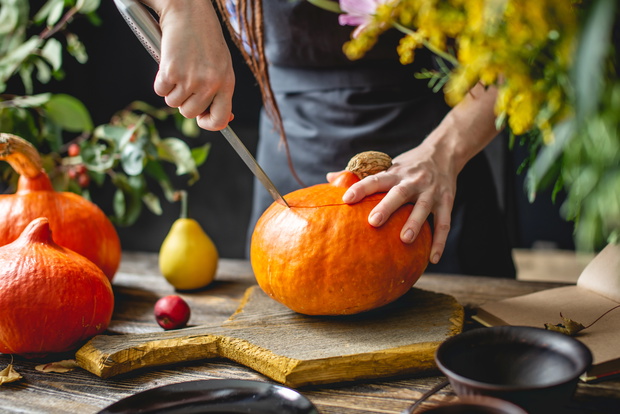 Woman chef cleans an orange pumpkin to prepare for baking. Autumn food in a cozy dark wooden kitchen with yellow flowers