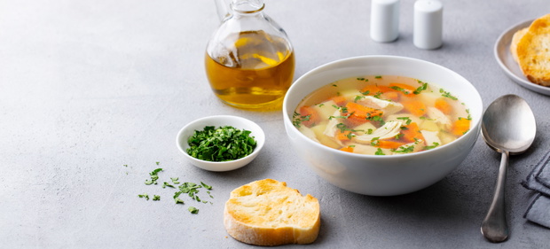 Chicken soup with vegetables in white bowl. Grey stone background. Copy space.
