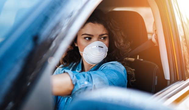 Young woman driving car with protective mask on her face.  Healthcare, virus protection, allergy protection concept.