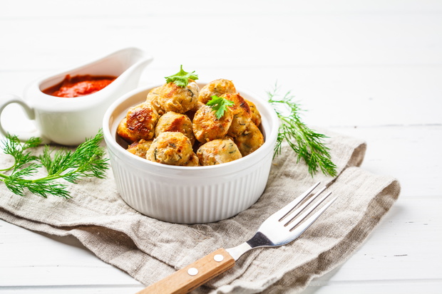 Healthy chicken meatballs with greens and tomato sauce on white background.