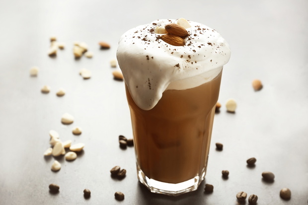 Glass of iced coffee and nuts on grey background