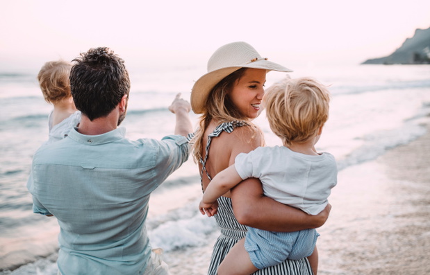 A family with two toddler children walking on beach on summer holiday at sunset.