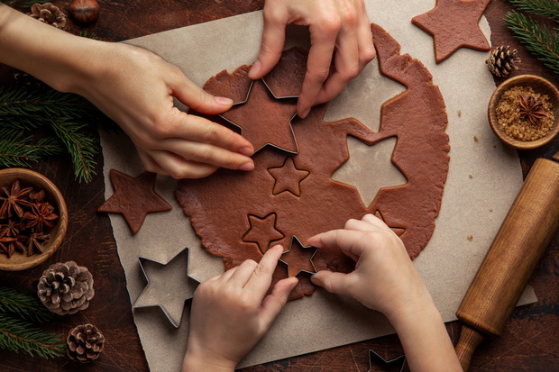 Christmas and New Year bakery. Close up of kids and female hands cooking traditional gingerbread cookies. Wooden kitchen table.