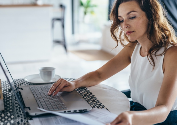 Woman using laptop while sitting at table. Young businesswoman sitting in kitchen and working on laptop.