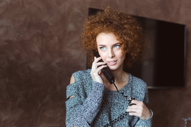 Portrait of pretty smiling redhead curly young female using telephone