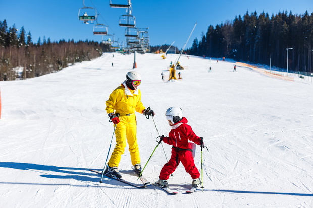 Mother and daughter having fun and learning skiing making first steps with mom's support on a ski winter resort at mountain hill.