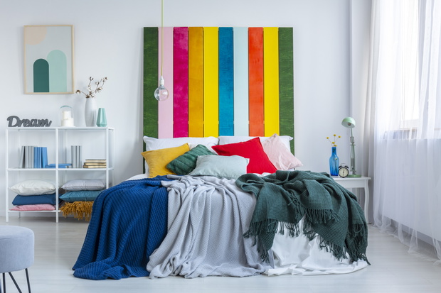 Green, gray and blue blankets on a white bed with rainbow bedhead in white, scandi bedroom interior. Real photo