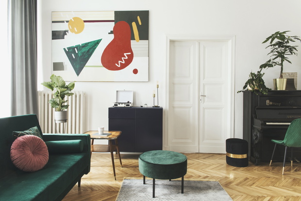 Luxury home interior with design velvet sofa, armchair, tables, pouf, commode and accessroies. A lot of plants on the piano. White walls with painting. Sunny view. Stylish decor of sitting room.