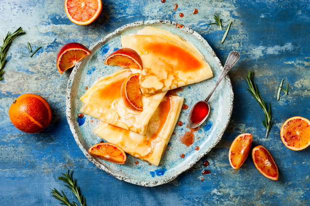 Homemade crepes pancakes served in ceramic plate with  orange sauce. French Crepe Suzette with bloody oranges and rosemary syrup.