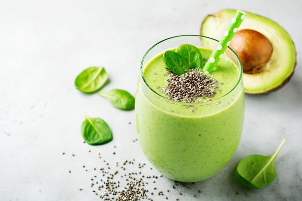 Vegetarian healthy green smoothie from avocado, spinach leaves, apple and chia seeds on gray concrete background. Selective focus. Space for text.