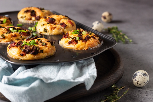 Savory muffins with bacon, quail egg, green onion cheese on a grey stone backdrop. Protein breakfast. Rustic style.