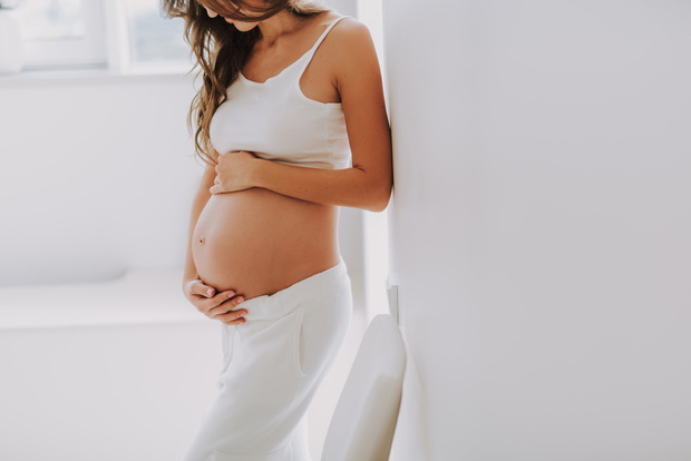 Pretty young woman holding hands on belly and looking down