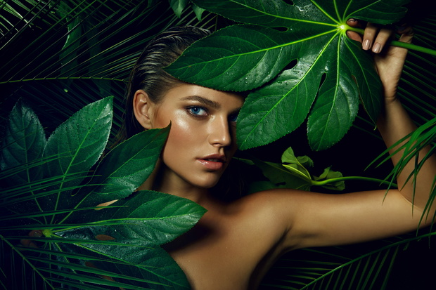 A beautiful tanned girl with natural make-up and wet hair stands in the jungle among exotic plants.