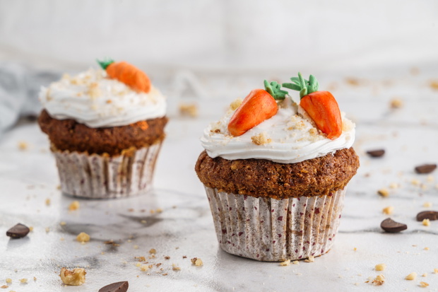 Easter cupcakes or muffins with cream and carrot candy on light marble background. Holiday cake celebration, delicious dessert, close up