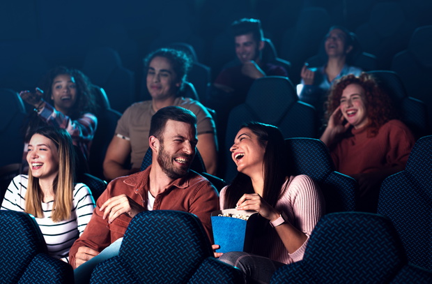 Group of cheerful people laughing while watching movie in cinema.