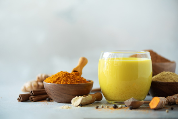Hot healthy drink. Turmeric latte, golden milk with turmeric root, ginger powder, black pepper over grey background. Copy space. Spices for ayurvedic treatment. Alternative medicine concept.