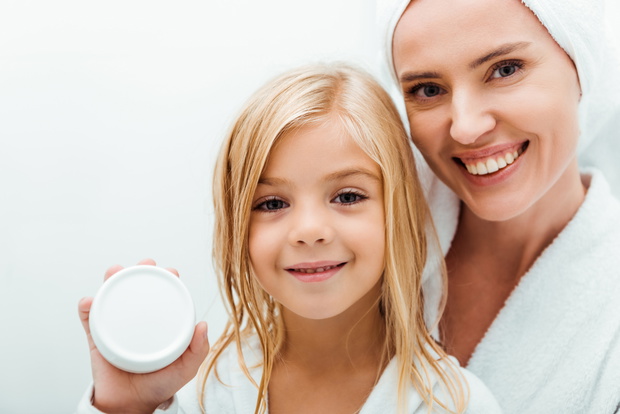 cute kid holding container with cosmetic cream near cheerful mot