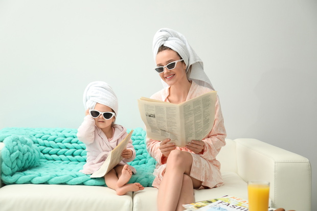 Mother and little daughter in bathrobes with newspapers sitting