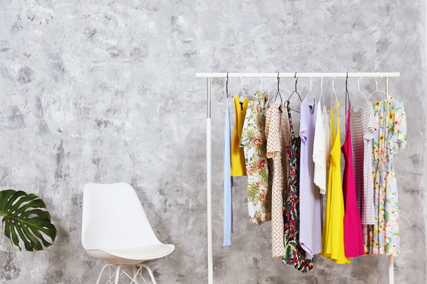 Women's hip clothing store interior concept. Row of different colorful female clothes hanging on rack in hipster fashion show room in shopping mall. Grunged concrete wall background. Copy space.