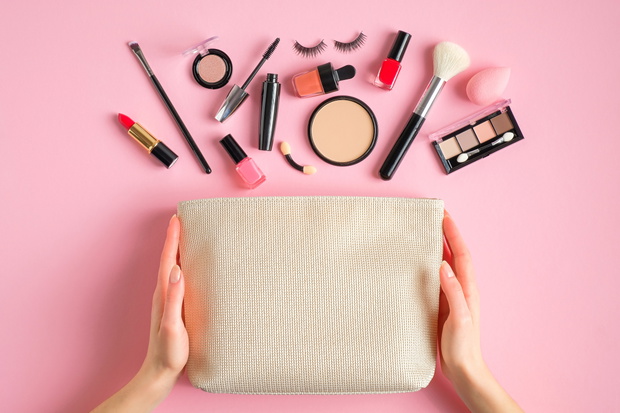 Female hands holding makeup bag with cosmetic beauty products ov