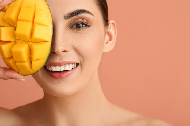 Beautiful woman holding cut mango on color background