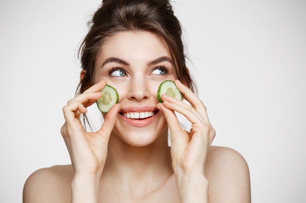 Young beautiful girl with perfect clean skin smiling holding cucumber slices over white background. Beauty cosmetology and spa.