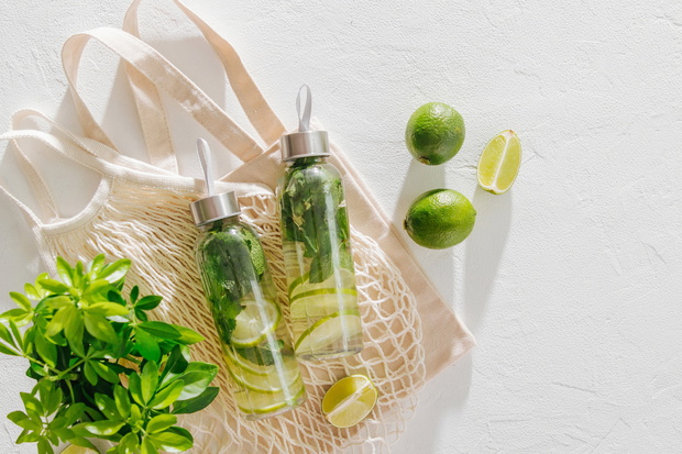 Fresh lime and mint infused water, cocktail, detox drink, lemonade in reusable bottles with eco bags. Eco friendly. Sustainable lifestyle.