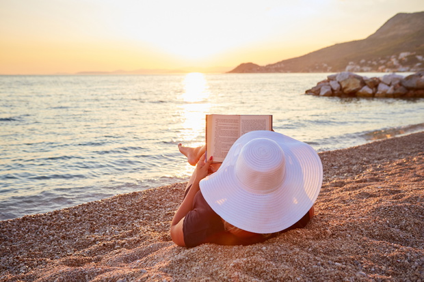 Woman reading a book on the beach at sunset