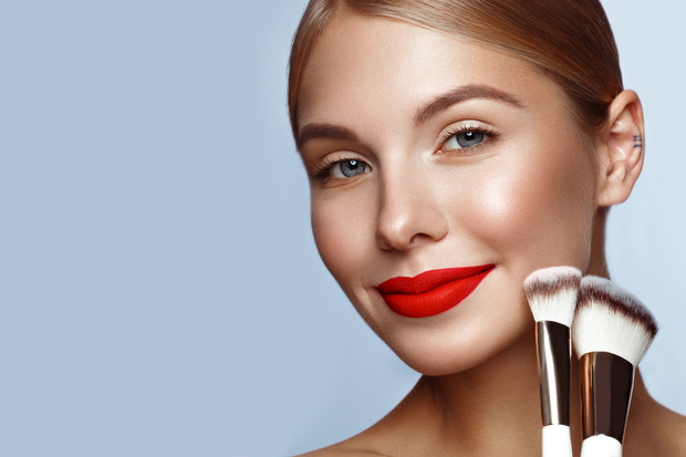 Beautiful girl with red lips and classic makeup with cosmetic brushes in hand. Beauty face.